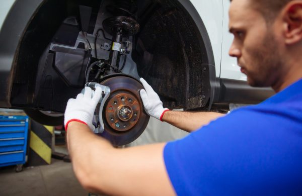 Young auto mechanic in a special suit repairs the brake system of a car or changes the brake pads
